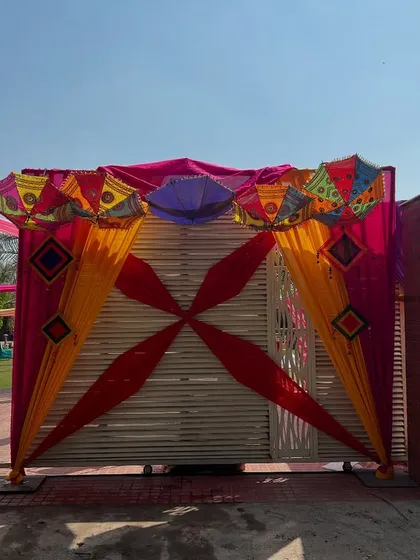 A festive entrance gate for an outdoor event, decorated with colorful drapes, Rajasthani umbrellas, and traditional hangings.