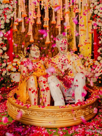 A wide shot of the couple seated in traditional urns, being showered with petals during their fun-filled Haldi.