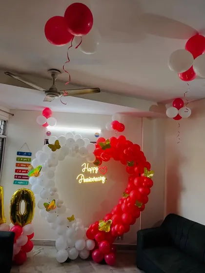 Celebrate your love with a classic anniversary decoration. This heart-shaped balloon arch, made of red and white balloons with butterfly accents and a "Happy Anniversary" neon sign, is perfect for home celebrations.