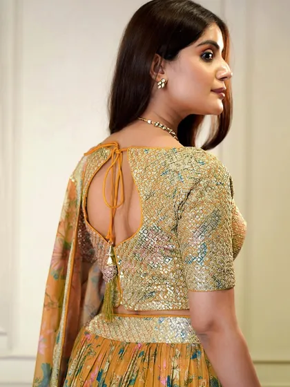 A pop of color for your celebration. This orange organza lehenga with a sequined blouse and floral skirt is designed for a fun and festive event like a Haldi or Sangeet.