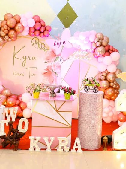 A full stage setup for a butterfly-themed 2nd birthday, with a custom backdrop, marquee 'TWO', and a pink and rose gold color scheme.