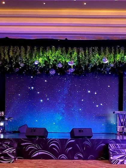 A stage set for a live band performance under a starry sky. The LED backdrop displays a galaxy of stars, while a canopy of greenery and disco balls adds a touch of glamour to the musical evening.