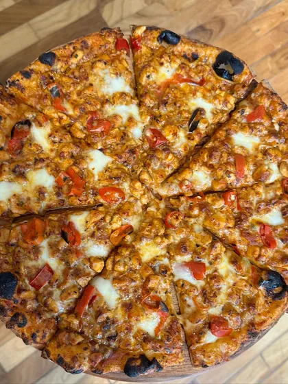 This is our popular peri-peri chicken pizza, sliced and ready to serve. The top-down view shows the generous toppings and the perfectly charred crust, a favorite at many of our catered parties.