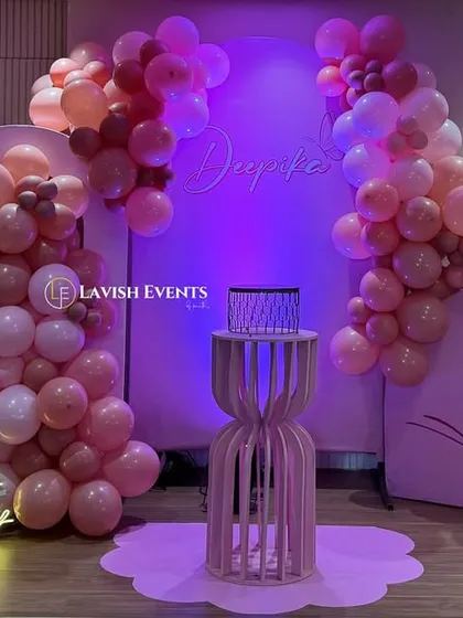 A whimsical butterfly-themed birthday setup. The decor includes pink balloon arches, butterfly cutouts, a neon "Happy Birthday" sign, and our stylish pink plinths.