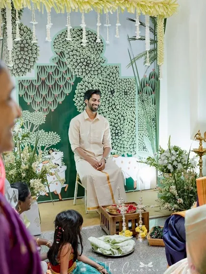 We specialize in creating beautiful at-home ceremonies. Here, a custom Pichwai-inspired backdrop and clean, green-and-white floral arrangements set a serene and artistic stage for an intimate Haldi.