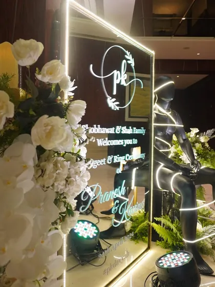 A modern welcome sign for a Sangeet and Ring Ceremony, featuring a custom monogram on a mirrored surface, lit with a neon-style border.