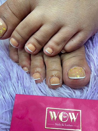A chic and stylish pedicure featuring toe extensions with a nude base, classic white French tips, and delicate gold foil accents. This is the ultimate in foot glamour.