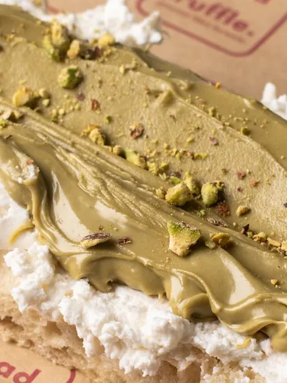 A close-up of a focaccia slice topped with creamy ricotta and pistachio spread. The texture and layers are the main focus of this appetizing shot.