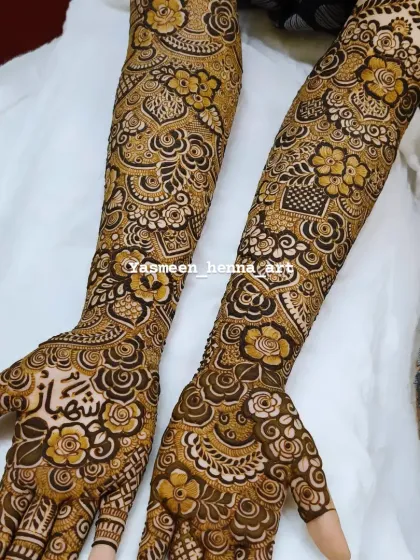 Hiba's mehndi, with the groom's name 'Shehbaz' beautifully written on her palm amidst a garden of henna flowers.