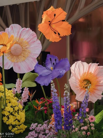 A close-up of the vibrant floral mandap, showcasing the variety of oversized paper flowers in shades of pink, orange, and purple, creating a rich and textured backdrop.
