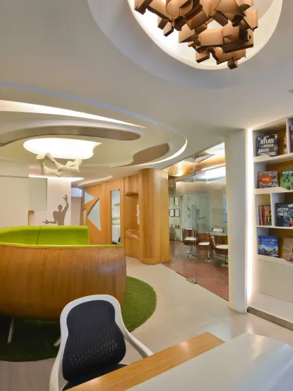 The reception desk in my studio is highlighted by a custom light fixture made of abstract wooden blocks. Opposite the desk, a bookshelf showcases our firm's projects, offering visitors a glimpse into our diverse portfolio.