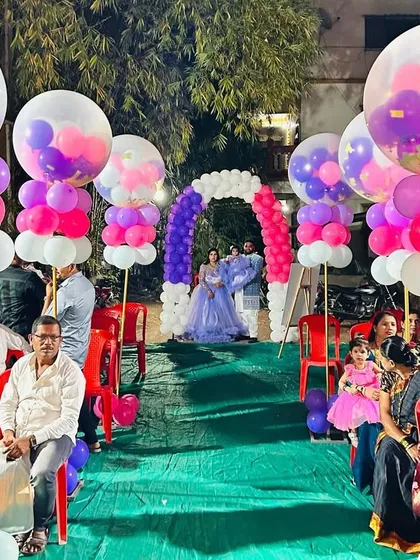 A beautiful balloon-lined walkway for an outdoor birthday party. The large confetti-filled balloons on pillars create a festive and elegant path for guests.
