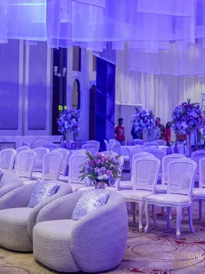 The guest seating area, featuring rows of elegant white chairs and modern lounge seating. The entire space is bathed in a soft purple light, creating a cohesive and magical atmosphere.