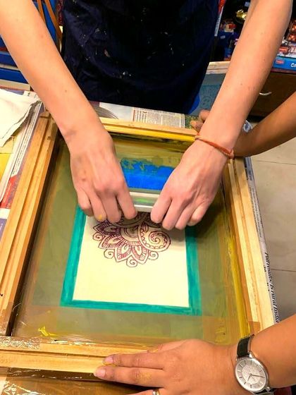 Two pairs of hands work together to pull the squeegee across the screen, ensuring an even layer of ink for a perfect print.