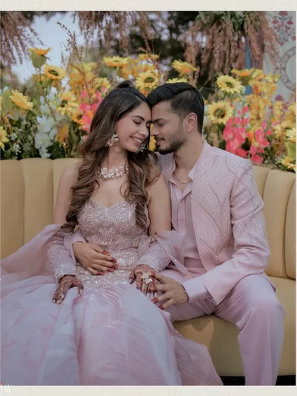 A tender moment between the couple, seated on a yellow couch against a backdrop of sunflowers. This intimate shot perfectly captures their connection amidst the vibrant decor of their Haldi carnival.