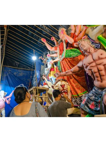Artisans work late into the night under a single bulb to complete a massive Durga idol, showcasing their dedication ahead of the festival.