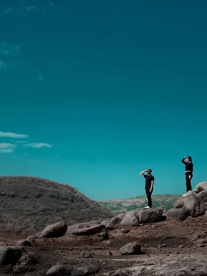 A wide, cinematic shot of the couple standing on rocks against a vast, deep blue sky. This kind of image emphasizes the scale of nature and the feeling of being on top of the world together.
