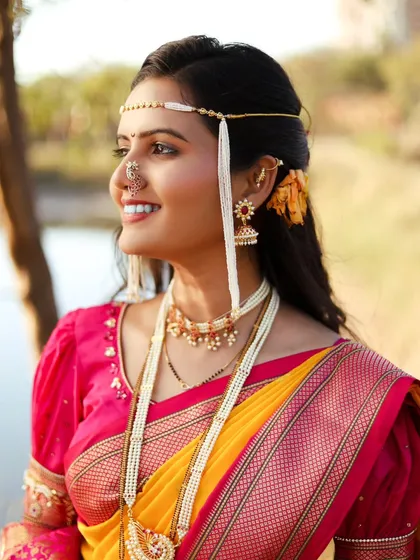 A joyful outdoor portrait of a bride in a traditional Maharashtrian Paithani saree. The natural light and green background make the bright yellow and pink of the saree stand out.