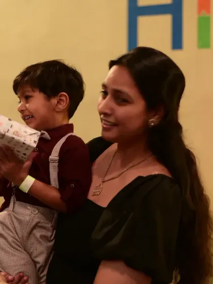 A mother holding her son as he opens a birthday gift. The excitement of presents is a highlight for any child.