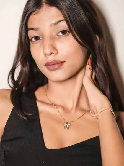 A detailed close-up on the model's face, capturing her soft makeup and the delicate butterfly necklace that contrasts with the dark dress.