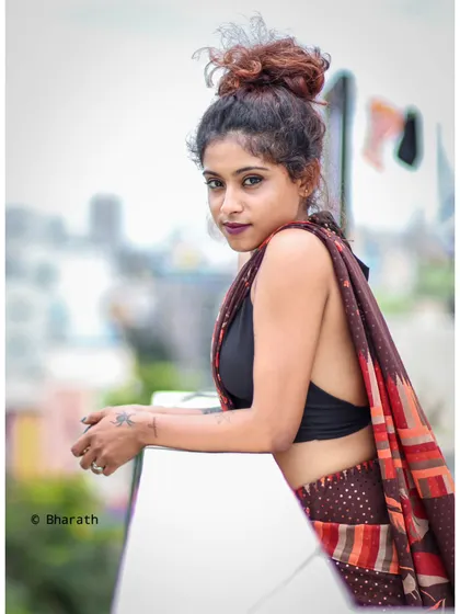 A modern fusion look, shot on a city rooftop. This image showcases a contemporary way to style a saree with a black halter top, blending traditional fabric with a bold, urban aesthetic against a blurred city backdrop.