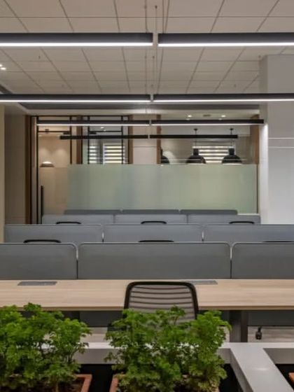 A view of the clean and organized workstation setup. The neutral color palette of the desks and dividers is complemented by the vibrant green of the plants, creating a balanced and calming workspace.
