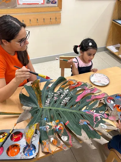 A large monstera leaf becomes a collaborative canvas for parents and children. This intergenerational art project allows for shared creativity, as different hands add layers of color and pattern, transforming a natural object into a collective masterpiece.