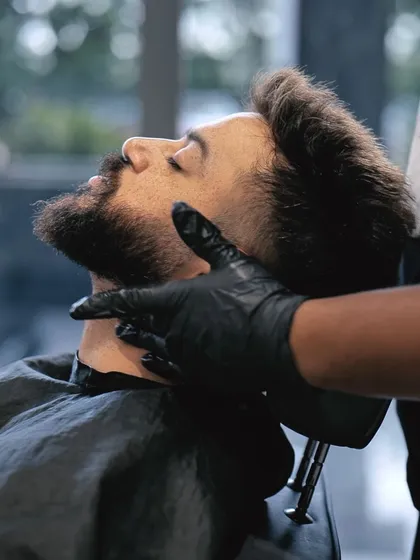 A client relaxing in the chair while receiving a beard trim, highlighting the relaxing aspect of our men's grooming services.