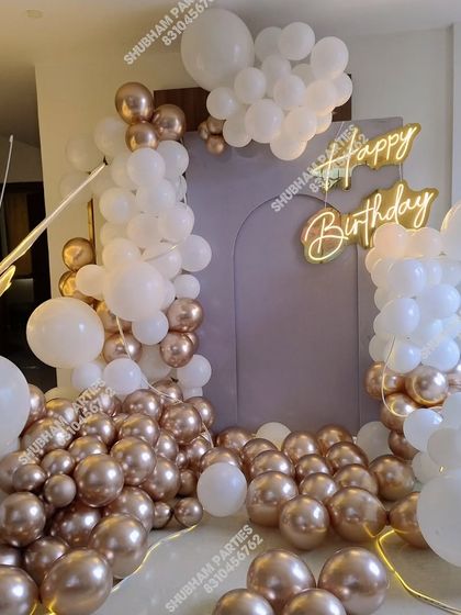 A sophisticated white and rose gold balloon arrangement with a large butterfly prop and neon sign.