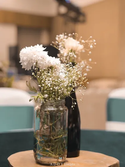 A minimalist centerpiece with white chrysanthemums and baby's breath in simple glass jars. This rustic-chic detail is perfect for more casual corporate events, workshops, or daytime functions.