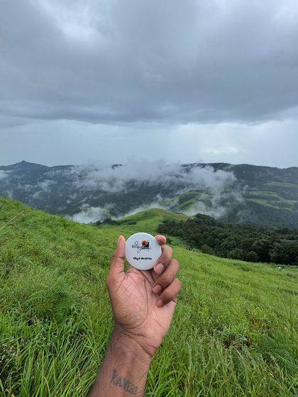 A hand holding our trek badge against the beautiful backdrop of the Gangadikal hills.