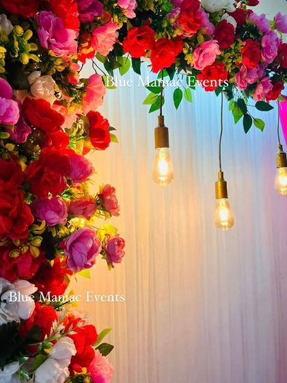 A close-up of the floral arch, showing the detail of the flowers and the warm glow of the Edison bulbs.