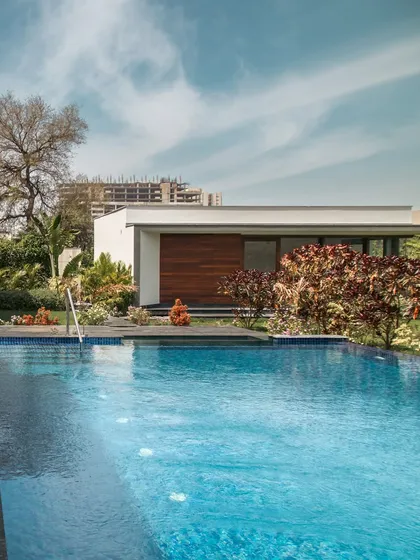 The pool and outhouse at Rosewood Farmhouse. The design prioritizes a strong connection to the outdoors, with the vibrant blue of the pool contrasting beautifully against the lush greenery and the clean, modern lines of the architecture.