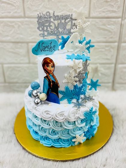 Let it go with a magical Frozen themed cake. This two-tiered design for a 4th birthday features Anna, a cascade of shimmering snowflakes, and a beautiful blue ombre frosting.