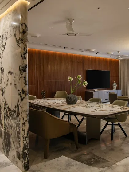 This residence is a sanctuary shaped by light, stillness, and balance. In the dining area, focus shifts toward a sculptural table that anchors the space, with a dramatic backlit marble partition separating it from the living area.