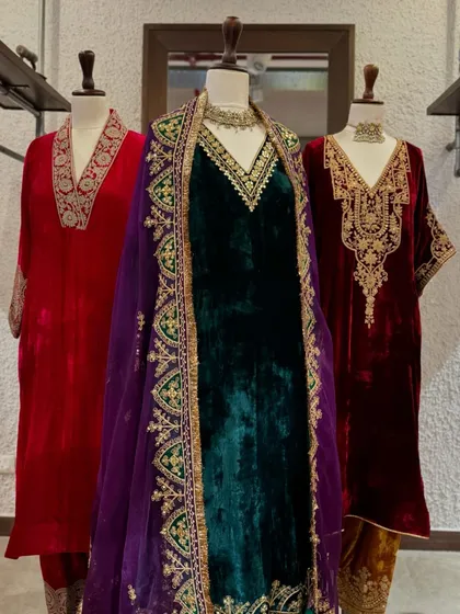 A wider view of the velvet collection, showcasing a stunning emerald green suit with a contrasting purple embroidered dupatta.