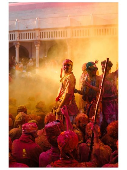 A man stands amidst a thick cloud of yellow and red Holi powder, the sunlight catching the particles in the air. The scene is both chaotic and beautiful, capturing the festival's atmosphere.