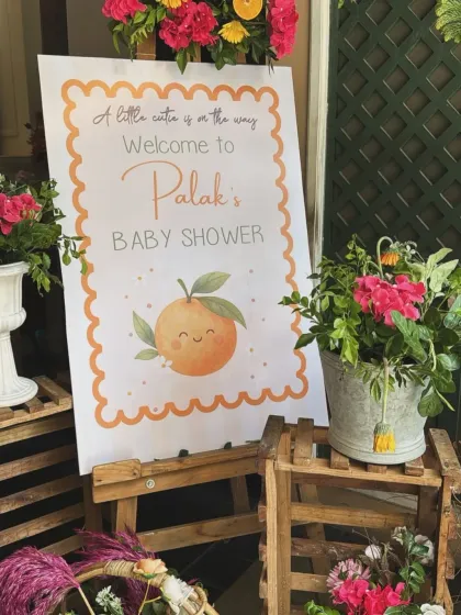 A personalized welcome sign for the 'Little Cutie' baby shower, set on an easel and surrounded by fresh flowers and rustic crates.