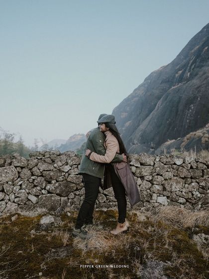 A warm hug against a backdrop of rolling hills and a stone wall, capturing the intimacy of their connection during this vintage-themed shoot.