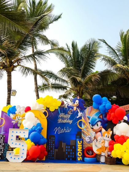 A dynamic Sonic the Hedgehog stage set against a beachside backdrop, with character cutouts, a city skyline, and a large marquee number '5'.