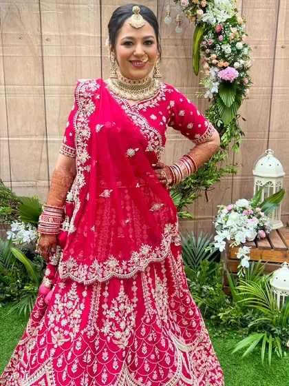 A full-length shot of this beautiful bride in her vibrant red lehenga. The makeup is balanced to stand out against the intricate outfit and the lush green background, creating a picture-perfect moment.