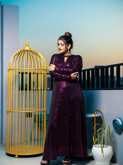 This shot showcases the elegant silhouette of the purple gown, with the model's makeup and top-knot hairstyle adding a touch of high-fashion sophistication.