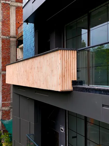 A close-up of the wood-finish fluted panels on a balcony, contrasting with the dark facade behind it. This detail showcases the warmth and texture that different materials bring to the design.