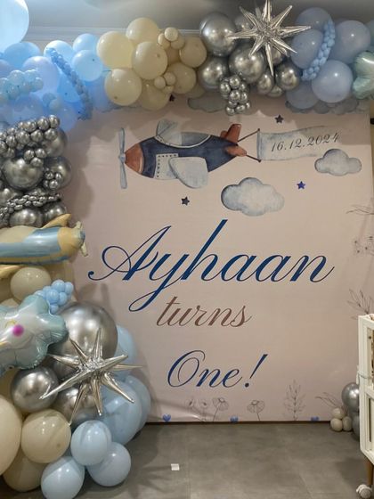 A clear photo of the airplane-themed first birthday backdrop for Ayhaan. The soft color palette and watercolor-style graphics create a gentle and charming atmosphere for a baby's first big celebration.