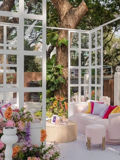 A cozy lounge pod at the "Bloom" wedding, featuring a pink sofa and colorful cushions, framed by a white grid structure and surrounded by flowers.