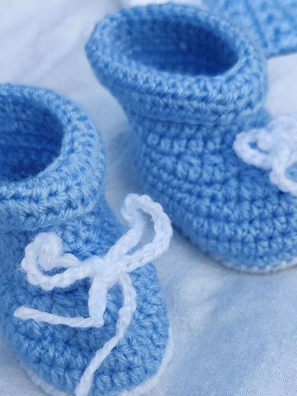 A complete newborn baby winter set in soft blue and white yarn. The set includes a cozy cardigan, pants with a drawstring, a pom-pom hat, and adorable little booties.