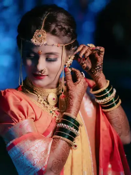 A close-up of the bride adjusting her earring, highlighting the detailed mehndi and traditional green bangles.