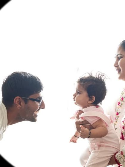 A different angle from the same backlit family session, showing the parents' joyful expressions as they interact with their baby.