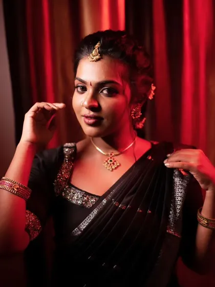 A dramatic portrait in a black saree. The red lighting adds a touch of mystery, while the makeup remains flawless and glowing.