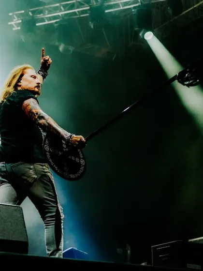 A powerful shot of a Dream Theater band member commanding the stage, raising his instrument to a roaring crowd.